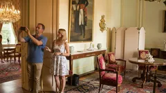 Turisté fotí interiér historického zámeckého pokoje s obrazy a starožitným nábytkem.