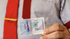 Muž v košili a kravatě drží v ruce český řidičský průkaz