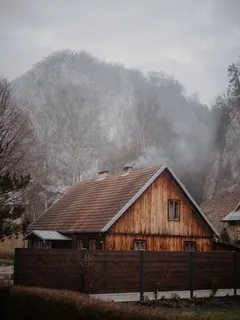 Hnědý dřevěný dům u stromů pod bílými mraky