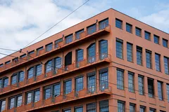 Červená industriální budova s velkými okny, modrá obloha, urbanistická architektura