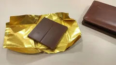 Čokoláda zabalená ve zlatém obalu položená vedle kožené peněženky na stole.