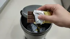 Ruka hází tabulku čokolády do odpadkového koše v kuchyni.