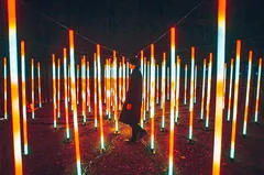 Osoba prochází instalací se zářícími tyčemi v noci, moderní umělecká světelná expozice.