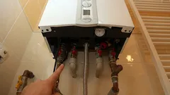 Montáž plynového kotle v koupelně, instalatér ukazuje na přívodní potrubí.