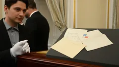 Kurátor drží rukavici vedle historických dokumentů vystavených na podstavci v interiéru.