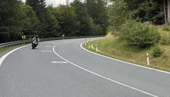 Motorkář projíždí zatáčkou na silnici obklopené lesem za denního světla.