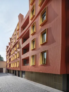 Moderní bytový dům s červenou fasádou a žlutými rámy oken, architektura Praha