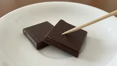 Dvě tabulky tmavé čokolády na bílém talíři, jedna propíchnutá špejlí.