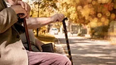 Dva senioři s holí sedí na lavičce v parku na podzim